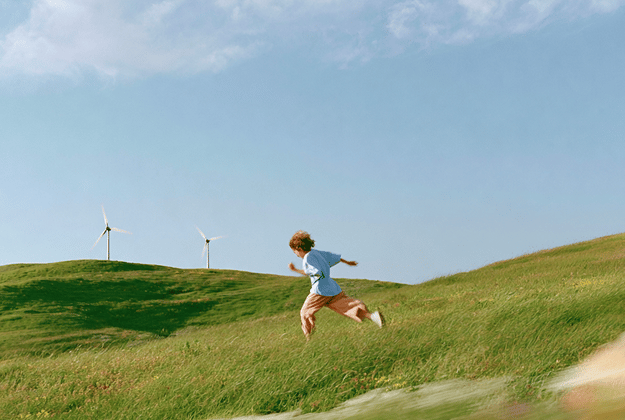 A child running down a grassy hill past wind turbines