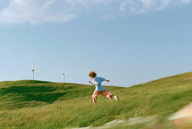 A child running down a grassy hill past wind turbines